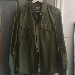 Olivgrön skjorta från Glanshirt - Säljer en stilren olivgrön skjorta från Glanshirt, tillverkad i Italien. Skjortan har långa ärmar och knappar framtill samt på axlarna. Ny pris över 3000, Den sitter som en M. Hör av er vid funderingar 