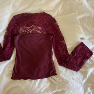 Vinröd spetsblus från Venderby’s - Elegant vinröd spetsblus från Venderby med långa ärmar och ett transparent mönster. Perfekt att ha slm festtopp. I st M/L. Oanvänd med lappar kvar.