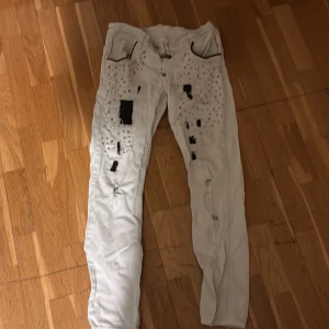 Vita jeansbyxor från Philipp Plein - Unika vita jeansbyxor från Philipp Plein med slitna detaljer och nitar. Byxorna har en straight cut och är tillverkade i Italien. De har svarta dragkedjor vid fickorna och en tydlig logotyp på baksidan. Pris är  absolut diskuterbart, lite osäker på storleken men det står och jag har tagit bild