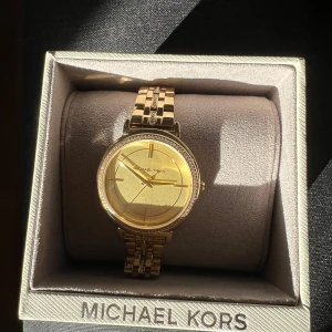Michael Kors klocka - Säljer guldfärgad Michael Kors klocka i nyskick och har endast använts ett fåtal gånger. Stilren och elegant design med glittrande detaljer både runt urtavlan och på armbandet. Extra spännen medföljer för att justera längden på armbandet.
