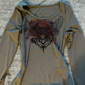 grön långärmad topp med tryck - Säljer en grön långärmad topp med ett coolt tryck av vingar och stjärnor i rött och svart. 