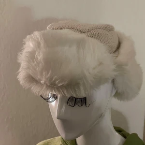 Vit vintage pälsmössa - Ascool beige / vit vintage pälsmössa som man kan knyta upp snörena på huvudet till en pälshatt (bild 1) eller knyta under hakan (bild 2). Fuskpäls och stickad. gosig o varm!!🤍🤍🐻‍❄️Normalstor, passar nog de flesta huvuden. 