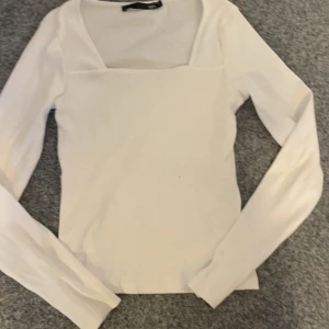 Vit ribbad topp från 157 - Säljer en stilren vit ribbad topp från 157 i storlek S. Toppen har en fyrkantig halsringning och långa ärmar, perfekt för en enkel och snygg look. Passar bra till både jeans och kjol.