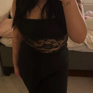 Svart spetsdetaljerad tubtopp - Snygg svart tubtopp med spetsdetaljer i midjan. Perfekt för en kväll ute eller en speciell tillställning. Toppen är ärmlös. Ny och oanvänd!