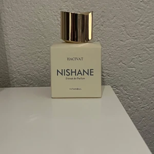 Hacivat Extrait de Parfum från Nishane - Säljer en elegant flaska av Hacivat Extrait de Parfum från Nishane, som jag fick i present på min 18 årsdag. Säljer den på grund av att lukten inte riktig passade mig. Den är knappt använd och i princip helt full. Flaskan är vit med en stilren design och har en gyllene kork. Parfymen kommer i en lyxig svart förpackning med guldfärgad text. Perfekt för den som söker en magisk doftupplevelse.