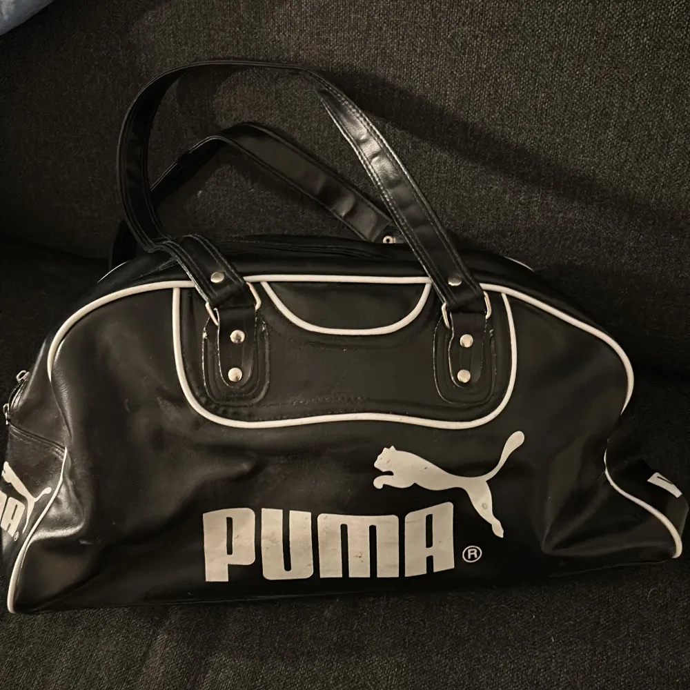 Snygg svart axelväska från Puma med vita detaljer och logga. Väskan har en praktisk dragkedja upptill och rymligt inre. Perfekt för att bära med sig det nödvändigaste med stil.. Laukut & Käsilaukut.