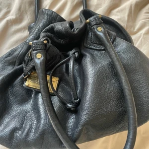   Marc by Marc Jacobs - Säljer en snygg svart väska från Marc Jacobs. Väskan har en cool och rymlig design med två handtag och guldfärgade detaljer. Perfekt för både vardag och fest! sååå snygg🥰🥰