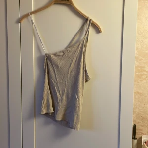 Beige ribbad linne - Säljer en snygg beige linne med ribbad textur. Den har en asymmetrisk design med en axelbandslös stil på ena sidan och en smal axelrem på andra sidan. Perfekt för sommardagar eller en avslappnad festkväll. Superbekväm och lätt att matcha med jeans eller kjol! kostar endast 40kr. från Cubus. fler bilder skickas om du vill.💕