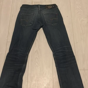 Mörkblå jeans från Replay - Säljer ett par snygga mörkblå jeans från Replay. De har en klassisk femficksdesign och en cool detalj med en metallplatta vid fickan. Jeansen är i bra skick och perfekta för både vardag och fest. Passar till allt!