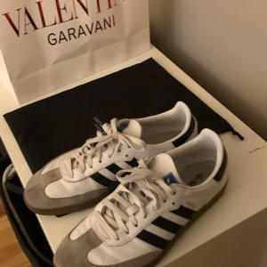 Adidas Samba sneakers - Säljer ett par klassiska Adidas Samba sneakers i vitt och grått med svarta ränder. Skorna har en snygg retrostil med snörning och är i väldigt bra skick. pris endast 799
