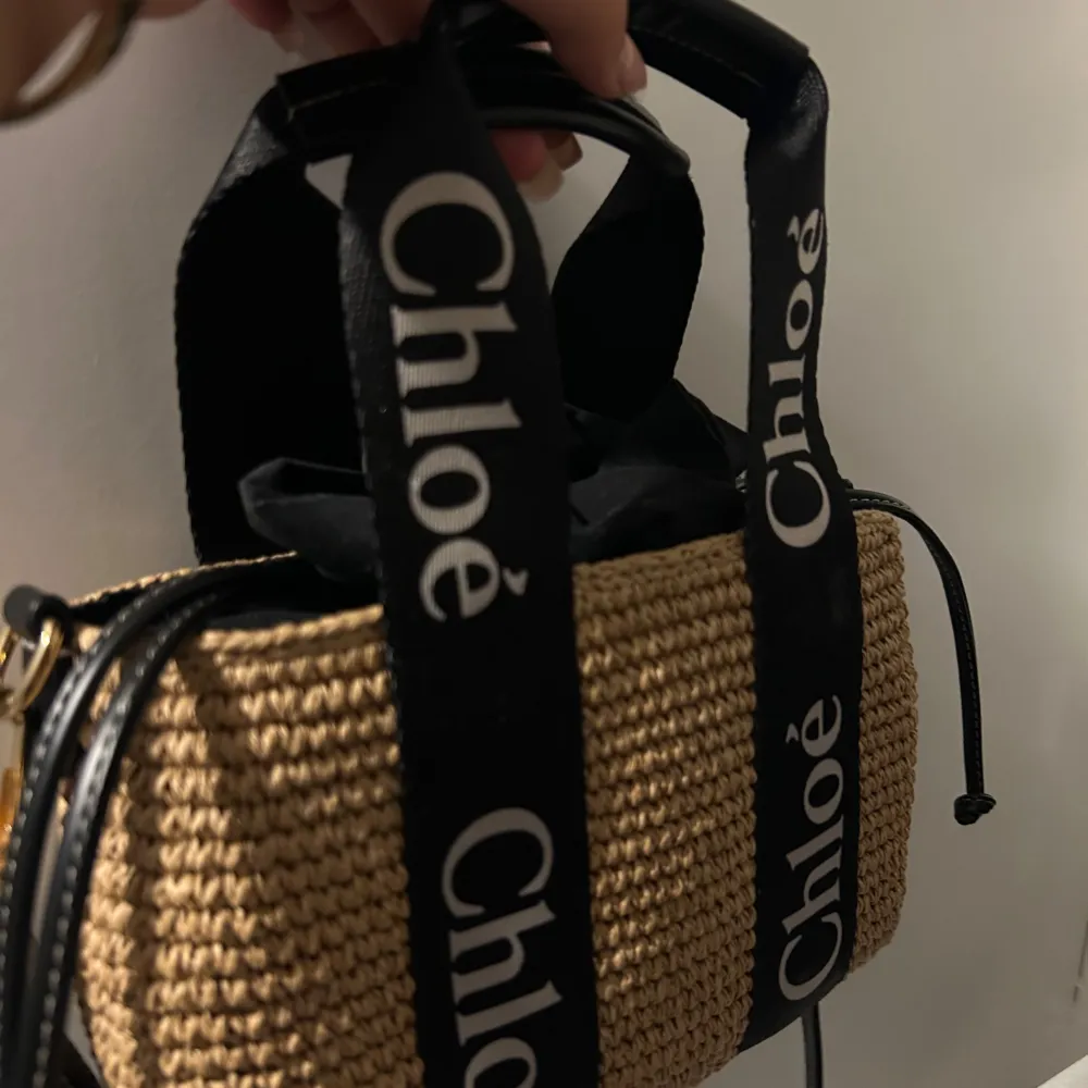 Säljer en superfin beige väska från Chloé. Den är gjord i ett flätat material som ger en snygg och somrig look. Väskan har svarta handtag med Chloé-loggan tryckt i vitt, vilket ger en cool kontrast. Perfekt för både vardag och fest!. Laukut & Käsilaukut.