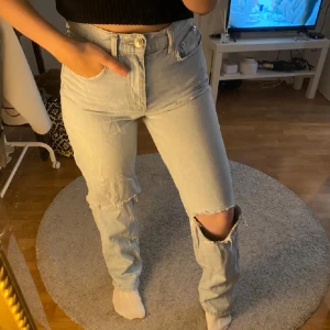 Ljusa jeans med slitningar - Säljer ett par ljusa jeans från Gina tricot i storlek 36. De har en snygg slitning på knäna som ger en cool och avslappnad look. Perfekta för vardagsbruk eller en avslappnad utekväll. De är i bra skick och har en klassisk femficksdesign.