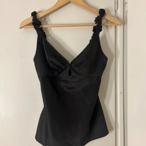Svart satinlinne med rynkade axelband - Säljer en så fin satintop från Adoore, sitter jättefint på men är lite stor på mig. 