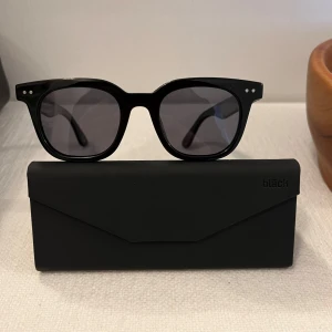 Svarta solglasögon från Marc - Säljer ett par snygga svarta solglasögon från Marc/Bläck. De har en klassisk fyrkantig form med mörka linser och små silverdetaljer på bågarna. Perfekta för att ge en stilren look i sommar! Kommer med ett matchande svart fodral.