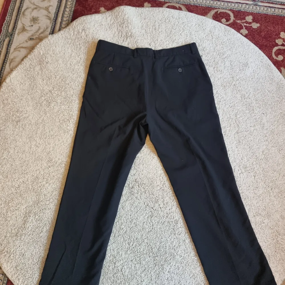 Säljer ett par stiliga svarta kostymbyxor från Batistini. De är gjorda av en skön blandning av ull och polyester med lite lycra för stretch. Byxorna har en klassisk rak passform och är perfekta för både formella tillfällen och kontoren.. Jeans & Byxor.