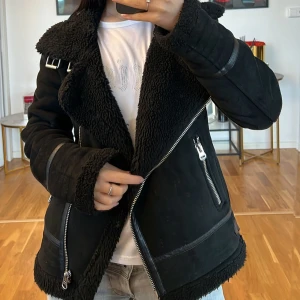 Svart jacka med teddyfoder Zara  💞 - Säljer en supercool svart jacka med teddyfoder. Den har en snygg dragkedja och flera detaljer som spännen och fickor med dragkedjor. Perfekt för höst och vinter när du vill hålla dig varm och stilren. Jackan har långa ärmar och en skön krage som du kan vika upp för extra värme.