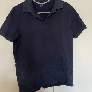 Mörkblå pikétröja från Uniqlo - Säljes en stilren mörkblå pikétröja från Uniqlo. Den har korta ärmar och en klassisk krage, perfekt för både vardag och lite mer uppklädda tillfällen. Tröjan är i bra skick och gjord av ett bekvämt material.