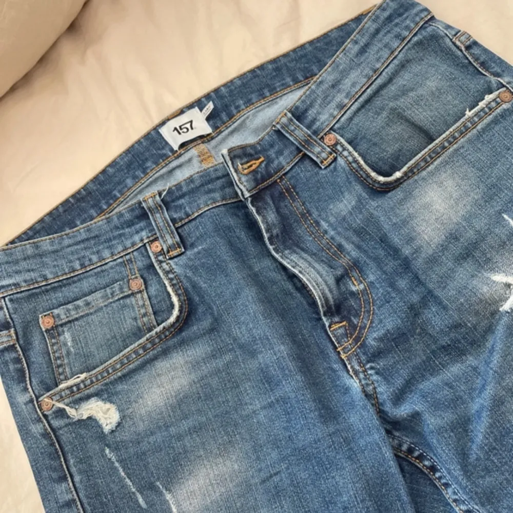 Säljer ett par snygga blå jeans med slitningar för en cool och avslappnad look. De har en klassisk femficksdesign och är perfekta för vardagsbruk. Jeansen har en normal passform och är tillverkade i ett slitstarkt denimtyg.. Jeans & Byxor.