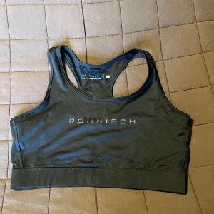 Svart sporttopp från Röhnisch - Säljer en svart sporttopp från Röhnisch i storlek L. Toppen har en stilren design med Röhnisch-loggan framtill. Perfekt för träning med sin bekväma passform och material som andas.