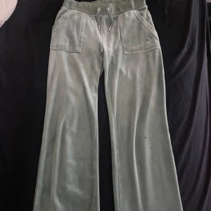 Gröna mjukisbyxor från Juicy Couture - Snygga gröna mjukisbyxor från Juicy Couture i en mjuk och skön velour. Byxorna har en hög midja med snörning och praktiska fickor med knappar bak. Perfekta för en avslappnad stil. Byxorna har några få fimphål, men inget som sticker ut särkilt mycket. Pris kan diskuteras