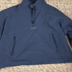 Mörkblå vindjacka från Aim'n - Säljer en mörkblå vindjacka från Aim'n i storlek S. Jackan har en hög krage och dragkedja framtill samt två praktiska fickor med dragkedjor. Materialet är en blandning av polyamid och elastan, vilket gör den både lätt och flexibel.