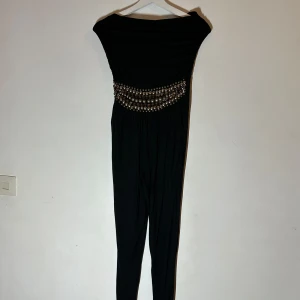Svart jumpsuit från Warehouse - Snygg svart jumpsuit från Warehouse med offshoulder-design och dekorativa pärlor i midjan. Perfekt för en kväll ute eller en speciell tillställning. Den har en elegant och stilren look som verkligen sticker ut.🥰🥰🥰