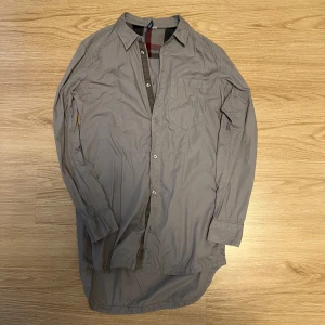 Beige långärmad skjorta - Säljer en stilren beige långärmad skjorta med knappar. Skjortan har en klassisk krage och ett diskret rutigt mönster på insidan av kragen. Perfekt för en avslappnad men ändå uppklädd look.