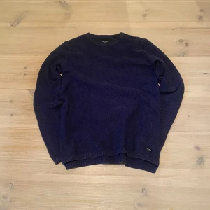 Mörkblå stickad tröja - Säljer en stilren mörkblå stickad tröja. Tröjan har en klassisk rund halsringning och långa ärmar. Perfekt för kyligare dagar och passar bra till både jeans och chinos. Ett måste i garderoben för den som gillar tidlös design. Skriv för frågor och mått osv