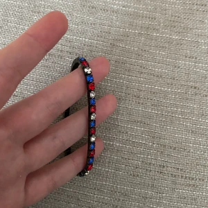Strass armband med stenar - Fint armband med glittrande stenar i rött, blått och silver 💙❤️🤍 Armbandet är elastiskt och passar de flesta handleder. Jättefint skick! 