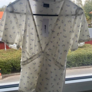 Vit blommig topp från Gina Tricot - Söt vit topp med blå blommor från Gina Tricot. Den har en djup v-ringning och korta ärmar. Perfekt för en somrig look!