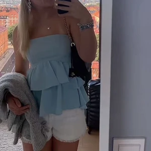 Ljusblå tubtopp med volanger - Säljer en söt ljusblå tubtopp med volanger. Toppen är axelbandslös och har en luftig passform, perfekt för varma dagar. Den ger en romantisk och somrig känsla.