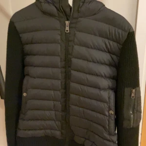 Svart cardigan från Moncler - Snygg svart cardigan från Moncler med quiltade detaljer och dragkedja. Jackan har en huva och en stickad struktur på ärmarna. Perfekt för kyligare dagar. Skick 10/10, använt fåtals gånger. Nypris runt 10 000kr. Pris kan diskuteras. L men passar bra som M.