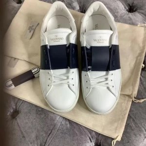 Valentino Garavani sneakers i vitt och blått - Snygga Valentino Garavani sneakers i vitt och blått. Skorna har en stilren design med snörning och de ikoniska nitarna. Den är typ nya har bara använt de några gånger och de är i jätte bra skick  har boxen med 👍