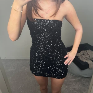 Svart paljettklänning - Snygg svart axelbandslös klänning täckt med glittriga paljetter. Perfekt för en kväll ute eller en fest. Från Nelly, storlek xs. Aldrig använd, säljer pga för kort  
