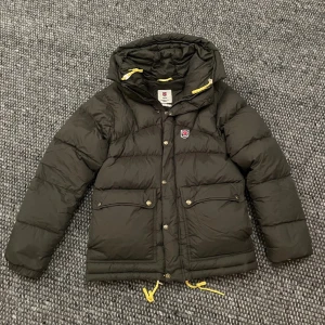 Grön dunjacka från Fjällräven - Säljer en grön dunjacka från Fjällräven med gula detaljer. Jackan är i nyskick endast använd några gånger och superfin. Perfekt för kalla dagar, storlek XS herr modellen. Priser går och diskuteras😊