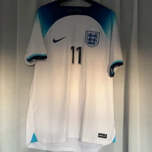  England fotbollströja Grealish  - Säljer en vit England fotbollströja från Nike med nummer 11 Grealish. Tröjan är från Unisport. Grealish använde flera nummer i england 2022 så den tröja har bara använt ett fåtal matcher. 