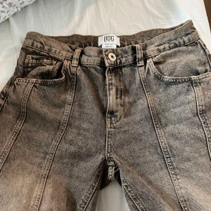 Grå jeans från BDG - Snygga grå jeans från BDG med en cool vintage-look. De har en broderad detalj på bakfickan och klassisk femficksdesign. Använda en gång men säljer pga av att dom är för stora. Pris kan diskuteras, ge gärna förslag
