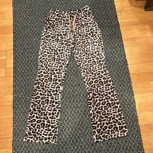 Leopardmönstrade byxor - Snygga leopardmönstrade byxor med hög midja och bootcut-stil. Perfekta för att sticka ut med ett djärvt mönster. Byxorna har en bekväm passform och är gjorda i ett mjukt material. Det finns även ett par praktiska fickor bak på byxan. Det finns en större röd fläck fram på byxorna.