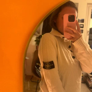 Vit stickad tröja från Stone Island - Säljer en snygg beige stickad tröja från Stone Island med hög krage och knappar framtill. Tröjan har en ikonisk logga på ärmen och ribbade muddar vid ärmslut och nederkant. Storlek M