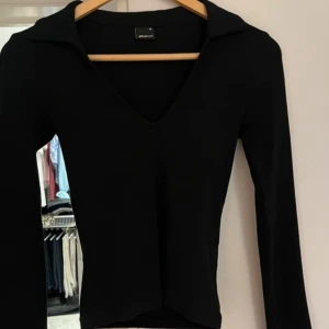 Svart långärmad tröja från Gina Tricot - Snygg svart långärmad tröja från Gina Tricot med v-ringning och krage. Perfekt för en stilren look. Passar bra till både jeans och kjol.