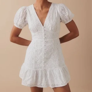 Vit klänning med spetsdetaljer - Köp ej via köp nu då den även ligger ute på vinted😇!!!!                                                                     Vit klänning med spetsdetaljer och puffiga kortärmar. Klänningen har en v-ringad design med knappar framtill och en volangkant nedtill. Använd endast två gånger. Perfekt för skolavslutningen!💖