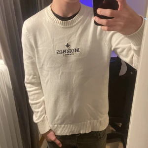 Vit tröja från Morris - Säljer en stilren vit tröja från Morris med broderad logga på bröstet. Tröjan har långa ärmar och ribbade muddar vid ärmslut och nederkant. Perfekt för en avslappnad look.