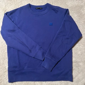 Lila collegetröja från Acne Studios - Säljer en stilren blå/lila collagetröja från Acne Studios. Tröjan har långa ärmar och en diskret logotyp på bröstet. Perfekt för en avslappnad look.