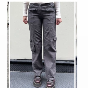 Gråa Cargobyxor - Snygga grå cargobyxor med flera praktiska fickor och en avslappnad passform. Perfekta för en cool och bekväm stil. Byxorna har en rak design och är tillverkade i ett slitstarkt material. Välanvända i fint skick!          Katt finns i hemmet🩷