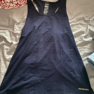 Mörkblå linnetopp från Newbody - Säljer en mörkblå linnetopp från Newbody i ett mjukt och stretchigt material. Toppen är ärmlös och har en enkel design med rund halsringning. Perfekt för träning eller avslappnade dagar. aldrig använd bara testad, lite ovetsized.