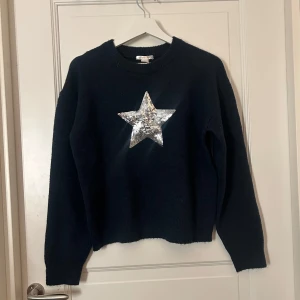 Mörkblå stickad tröja med stjärna - Säljer en mörkblå stickad tröja med en stor silverglittrig stjärna på framsidan. Tröjan har långa ärmar och en rund halsringning. Helt ny med prislapp! 🌟
