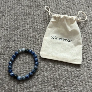 Blått armband från OneWear - Snyggt blått armband från OneWear med runda pärlor i olika nyanser av blått. Perfekt accessoar för att ge en färgklick till din outfit. Levereras med en praktisk tygpåse för förvaring. Limiterad 