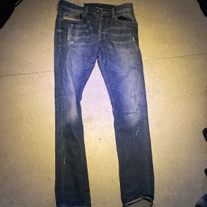 Blå jeans från Diesel - Snygga blå jeans från Diesel med en klassisk femficksdesign och slitna detaljer för en trendig look. Jeansen har en knappgylf och är perfekta för en avslappnad stil.