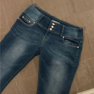 Blå jeans med knappar - Snygga blå jeans med flera knappar i midjan och klassisk femficksdesign. Jeansen har en diskret tvättad look och är perfekta för en avslappnad stil. De har en normal passform och är tillverkade i ett slitstarkt material.