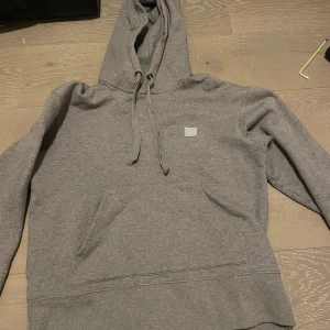 Grå hoodie från Acne Studios - Säljer en stilren grå hoodie från Acne Studios. Den har en klassisk design med en stor ficka framtill och justerbar huva med snören. Perfekt för en avslappnad look.